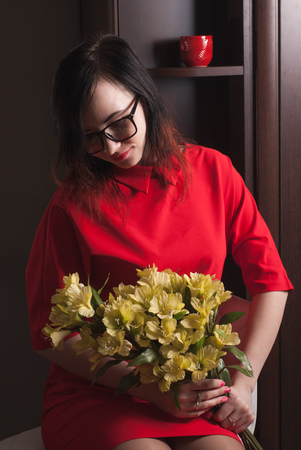 Girl in red dress with flowers, brunette with glasses holding a bouquet, photo in the dark keyの写真素材