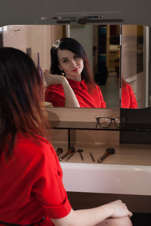 Woman in short red dress sitting in a chair in front of the mirror cute brunette in a classic styleの写真素材