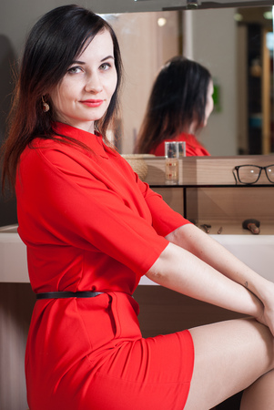Woman in short red dress sitting in a chair in front of the mirror cute brunette in a classic styleの写真素材