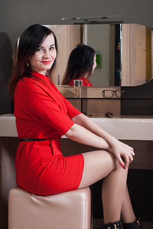 Woman in short red dress sitting in a chair in front of the mirror cute brunette in a classic styleの写真素材