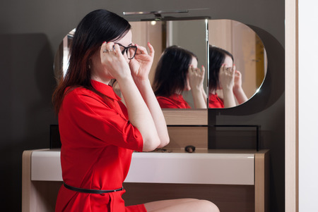 Woman in short red dress sitting in a chair in front of the mirror cute brunette in a classic styleの写真素材