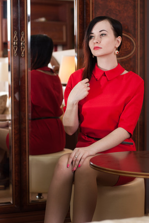 Beautiful girl sitting at a table in a red dress, an attractive young brunetteの写真素材
