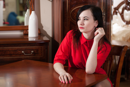 Beautiful girl sitting at a table in a red dress, an attractive young brunetteの写真素材