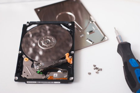 Took apart the hard drive from the computer, HDD drive, mirror effect, screwdriver with rubber handle, unscrewed the screws on a light backgroundの写真素材