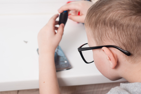 Little boy in glasses with a screwdriver, disassembly the hard disk, the boy busy, a young engineerの写真素材