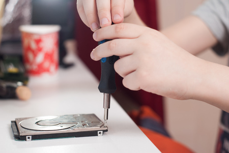 Hands of a little boy with the screwdriver, disassembling the hard disk drive, boy busyの写真素材