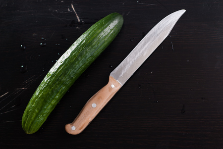 Fresh cucumbers and knife on a black cutting Board, the scratched surface,の写真素材