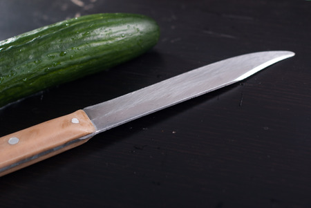 Fresh cucumbers and knife on a black cutting Board, the scratched surface,の写真素材