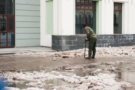 A man clears the sidewalk of ice, the worker of municipal services on the street, late spring, on the background of the Windows of the building,の写真素材