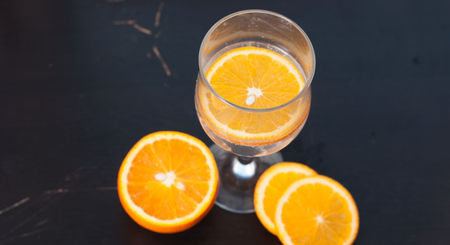 Orange slice in the glass, the view from the top, on a black wooden background, closeup, composition of sliced orangesの写真素材
