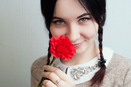 Playful girl holding a red carnation, flower in mouth, portrait of a girl with pigtails, cute brunetteの写真素材