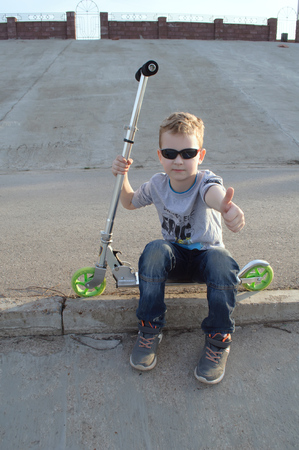 Little boy with sunglasses on a scooter, outdoor activities, tough guy showing thumb upの写真素材