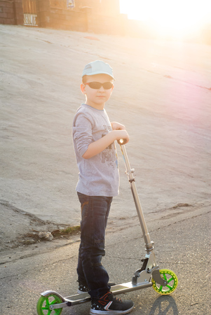 little boy in sunglasses and a cap riding a scooter, riding Sports, Sunset bright orangeの写真素材
