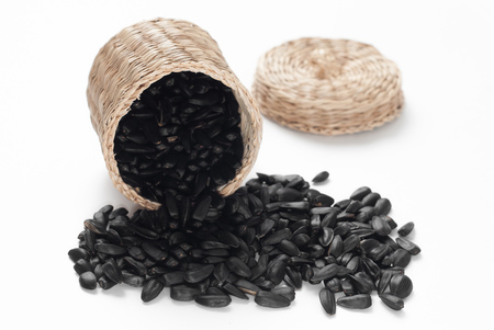 Sunflower seeds scattered on a white background, wicker basket with lid, roasted sunflower seedsの写真素材