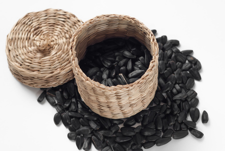 Sunflower seeds scattered on a white background, wicker basket with lid, roasted sunflower seedsの写真素材