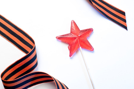 Lollipop in a star shape on white background, red candy on a stick, St. George ribbon, the symbol of the second world warの写真素材