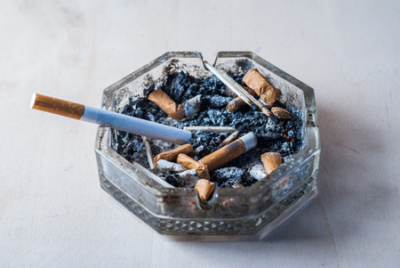 A cigarette with a filter in a dirty ashtray with cigarette butts, conceptual photography,の写真素材