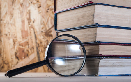 Magnifying glass and books, stacks of battered books on a wooden table. magnifier with black frameの写真素材