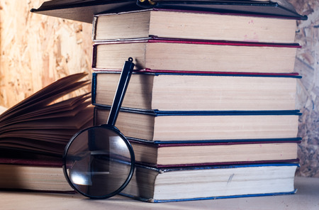Magnifying glass and books, stacks of battered books on a wooden table. magnifier with black frameの写真素材
