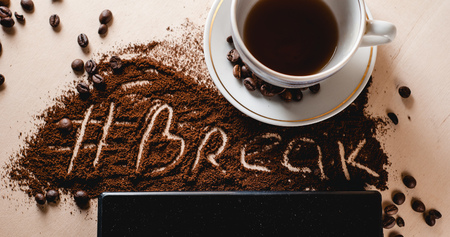 Cup with a hot beverage, roasted coffee beans close-up scattered on the Desk, digital tablet, lettering ground coffee hashtag breakの写真素材