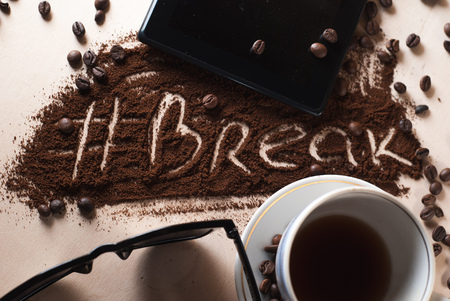 Cup with a hot beverage, roasted coffee beans close-up scattered on the Desk, digital tablet and points. decals ground coffee hashtag breakの写真素材