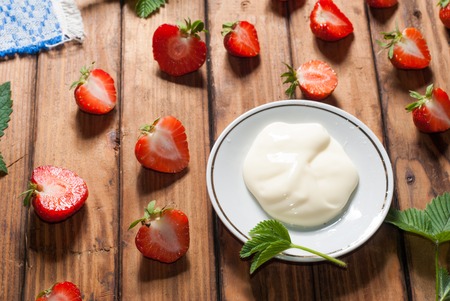 Strawberries with whipped cream, delicious dessert on wooden background, green leavesの写真素材