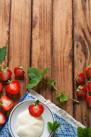 strawberries and whipped cream on old wooden table background, composition with freshly picked strawberries and leaves, copy space, healthy food, rustic styleの写真素材