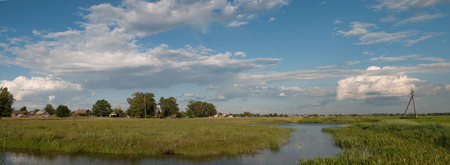The sky reflected in the water of an irrigation canal, the thick green grass around. the village and the distanceの写真素材