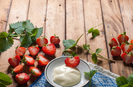 strawberries and whipped cream on old wooden table background, composition with freshly picked strawberries and leaves, copy space, healthy food, rustic styleの写真素材
