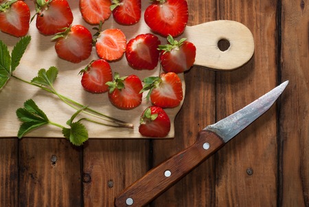 Fresh strawberries on a cutting Board and knife, arrangement of leaves and berriesの写真素材