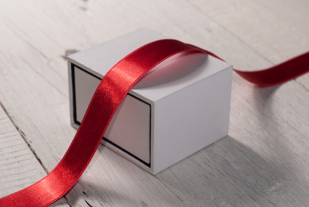 White box on wooden background. Gift box with red ribbon on wooden background with space.の写真素材