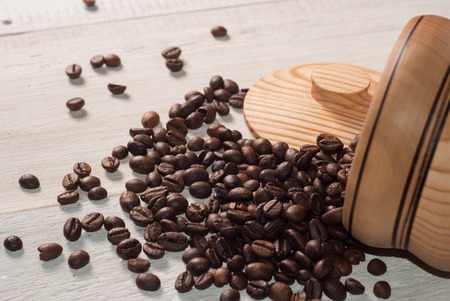 Coffee beans scattered from a Cup on white wooden background, wooden utensils, spilling the coffeeの写真素材