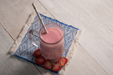 Strawberry milkshake in glass goblet with handle, straw from paper with stars, a smoothie with strawberries, embroidered napkin on wooden background, rustic styleの写真素材