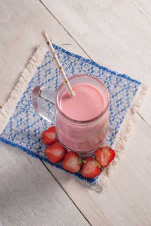Strawberry milkshake in glass goblet with handle, straw from paper with stars, a smoothie with strawberries, embroidered napkin on wooden background, rustic styleの写真素材