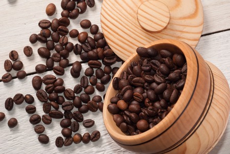 Coffee beans scattered from a Cup on white wooden background, wooden utensils, spilling the coffeeの写真素材