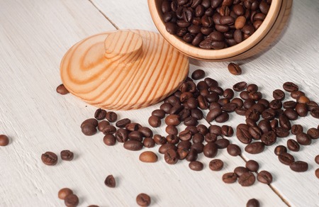 Coffee beans scattered from a Cup on white wooden background, wooden utensils, spilling the coffeeの写真素材