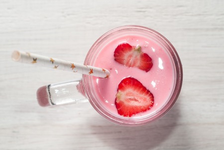 Smoothie with strawberries, pink cocktail with a straw on a white wooden table, top view,の写真素材