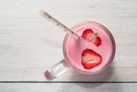 Smoothie with strawberries, pink cocktail with a straw on a white wooden table, top view,の写真素材