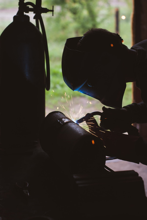 The silhouette of a welder, a tank of oxygen, bright lights and sparks, welding worksの写真素材