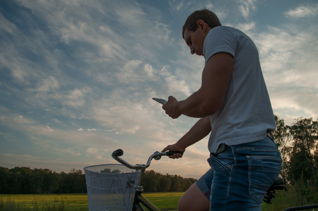 A cyclist looks at the phone against the sky, to seek the way in the Navigator, the journey on the bikeの写真素材