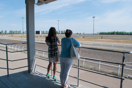 Women at the racetrack, people are watching horse racing, rear view, race track on a Sunny dayの写真素材