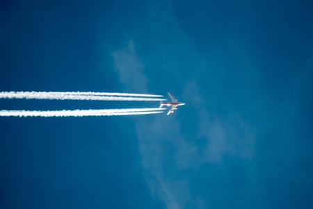 Silhouette of plane flying against the blue sky. A trail of smoke behindの写真素材