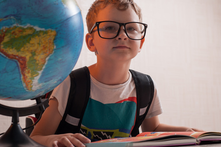Happy young schoolboy at his Desk in class , a geography lesson, a globe on the tableの写真素材
