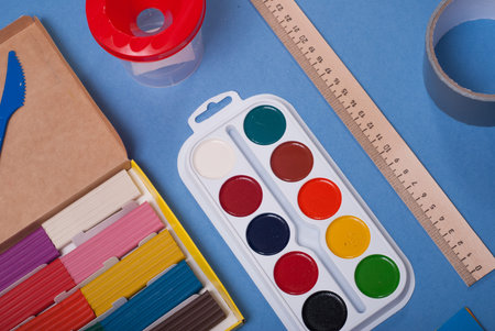 Set for a first grader, clay, paint, ruler on blue background, school supplies, back to school