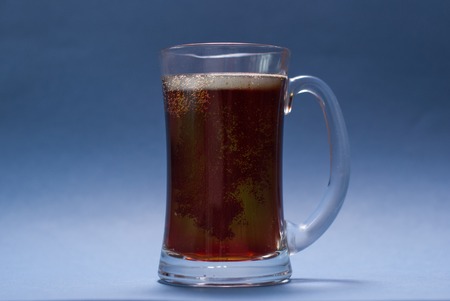 Glass mug with handle of dark beer on blue backgroundの写真素材