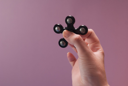Female hands with a popular toy fidget spinner. Spinning black spinner.Gadget anti stress on a pink backgroundの写真素材
