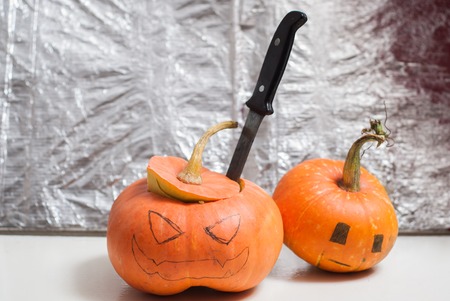 Jack-o-lantern DIY. to carve a pumpkin with a knife. the two pumpkins on the background of the foil. Halloween backgroundの写真素材
