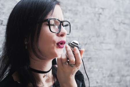 beautiful girl with glasses singing against a brick wall, singing into microphone at home Studioの写真素材
