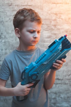 Little preschooler boy holding the Blaster with a dramatic face. Young actor with a toy gunの写真素材