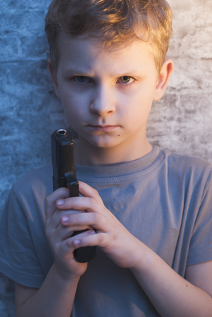 Boy with a gun in his hand against the brick walls, dramatic portraitの写真素材